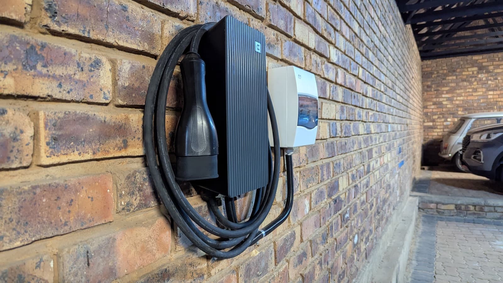 Tethered TeltoCharge with coiled cable on a brick wall